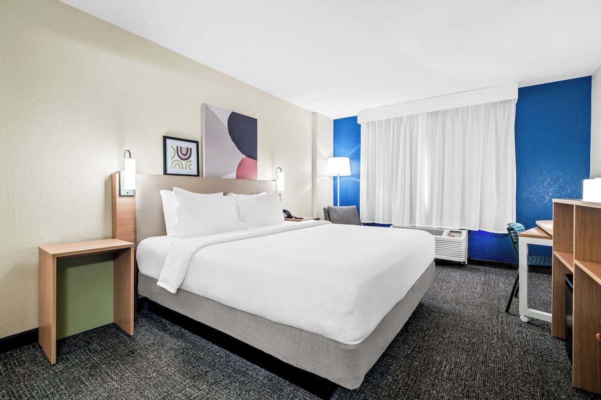 Ein Hotelzimmer mit einem Bett, Nachttischen, einem Schreibtisch, einem Sessel, einer Lampe und einem Wandbild.