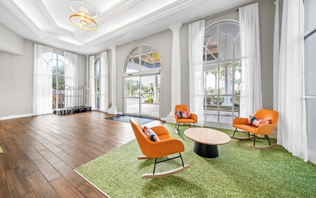 A spacious room with wooden flooring, large windows, and a green carpet. There are two orange rocking chairs and a round table.