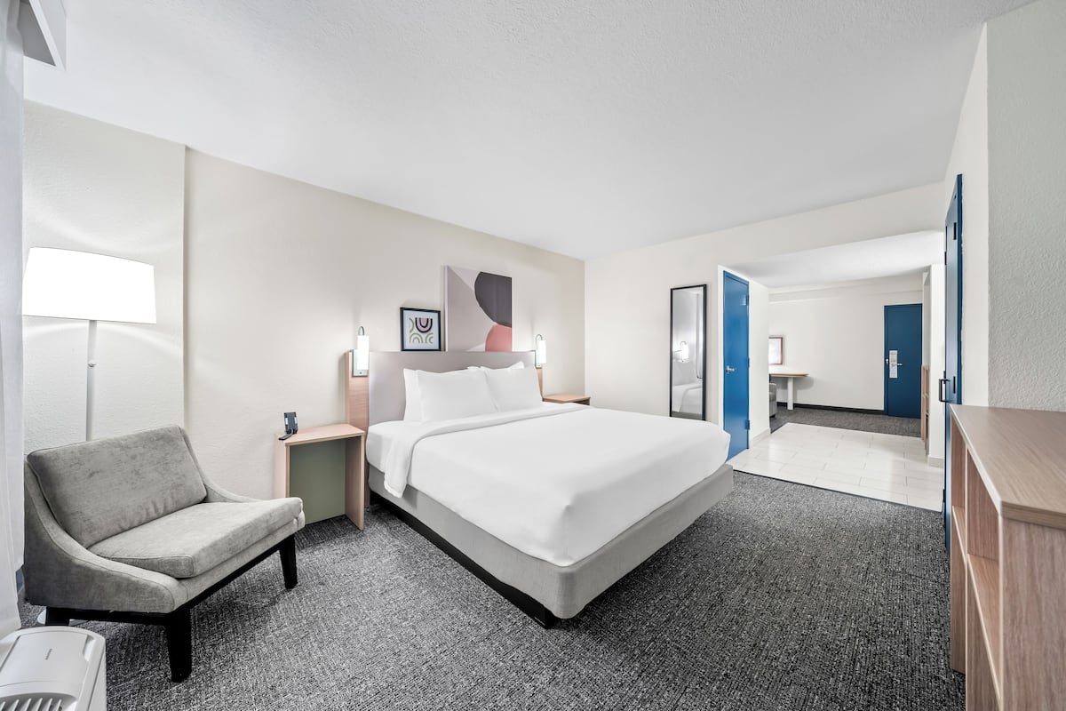 A hotel room with a bed, a chair, a desk, and a lamp.