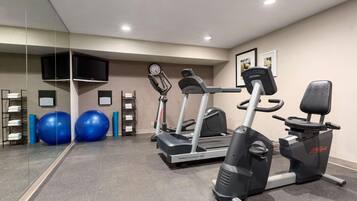 Un gimnasio con caminadora, elíptica y pelotas de ejercicio.
