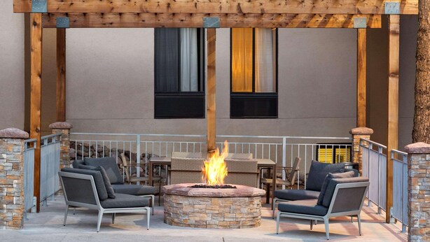 An outdoor patio with a stone fire pit, two grey sofas, and a wooden pergola.