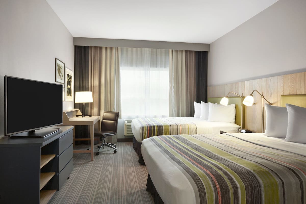 A hotel room with a flat-screen TV, a desk, two beds, a chair, and a large window with curtains.