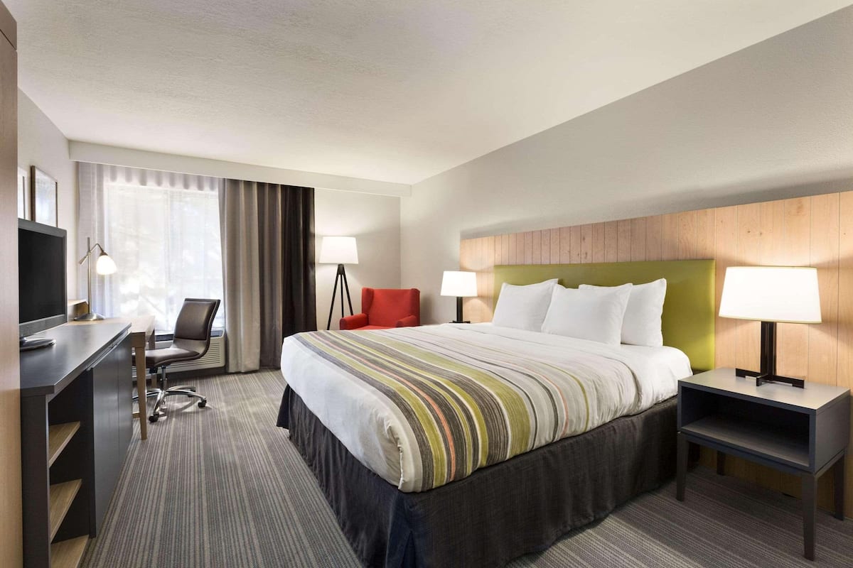 A hotel room with a bed, desk, chair, and lamps.