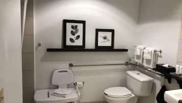 A small, modern bathroom with a toilet, bidet, and a shelf with framed pictures.