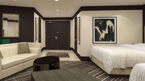 A hotel room with a white sofa, a bed, a small round table, and a large abstract painting on the wall.