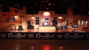 Un escenario con instrumentos musicales y una batería, un letrero de neón y un cartel con la marca 'Crown Royal'.