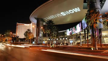 Un edificio moderno con un gran cartel que dice "FASHION SHOW" y palmeras en primer plano.