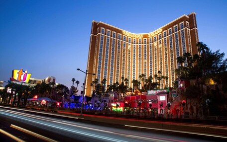 A large hotel with a curved facade and multiple floors, surrounded by palm trees and other buildings.