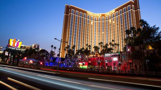 A large hotel with a curved facade and multiple floors, surrounded by palm trees and other buildings. - Treasure Island TI Las Vegas - Handwritten Collection (Las Vegas)