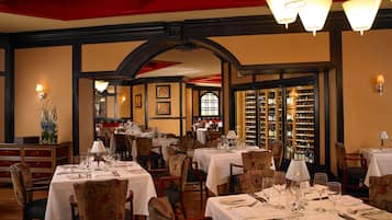 A restaurant with multiple tables set for dining, featuring a wine cellar visible through the glass doors.