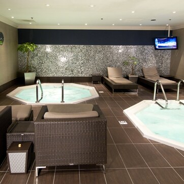 A spa area with two hot tubs, lounge chairs, and a towel rack.
