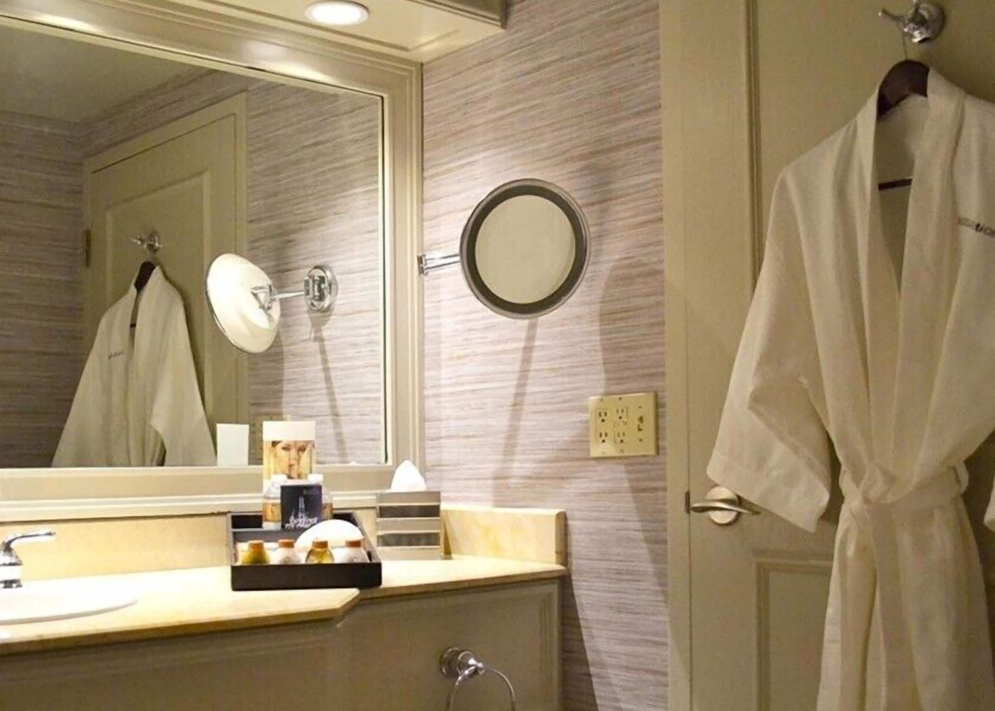 A bathroom with a large mirror, a round mirror, a towel rack, and a sink with toiletries.