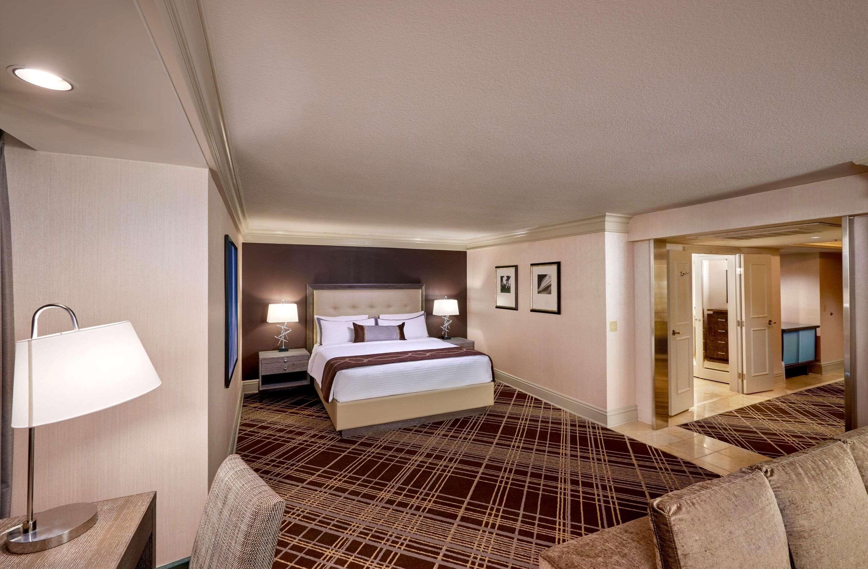 Ein Hotelzimmer mit einem großen Bett, zwei Nachttischlampen, einem Nachttisch, einem Sofa und Blick auf den Flur.