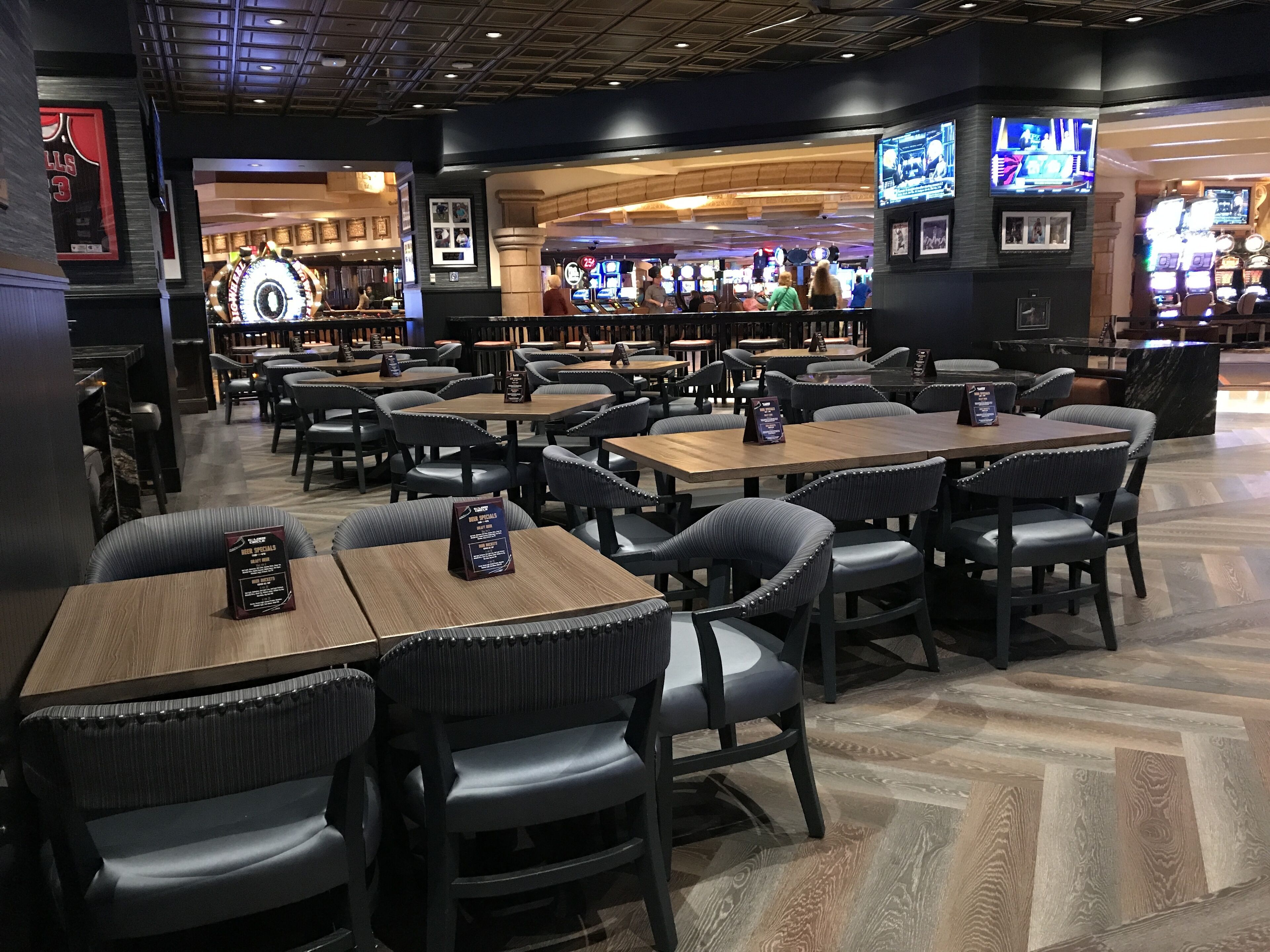 A restaurant with multiple tables and chairs, a bar area in the background, and various framed pictures on the walls.