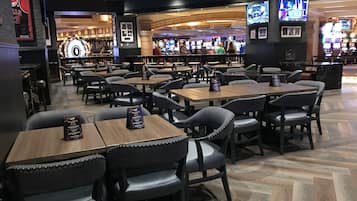 A restaurant with multiple tables and chairs, a bar area in the background, and various framed pictures on the walls.