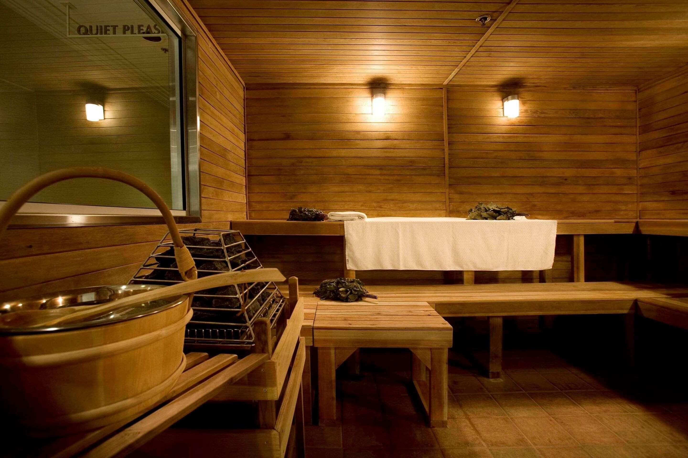 Un cuarto de sauna con bancos de madera, un banco con una toalla y un recipiente de madera grande.