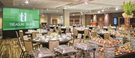 A banquet hall with round tables, buffet stations, and a large screen displaying "TREASURE ISLAND".