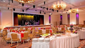 A banquet hall with round tables set for dining, a stage with musical instruments, and chandeliers.
