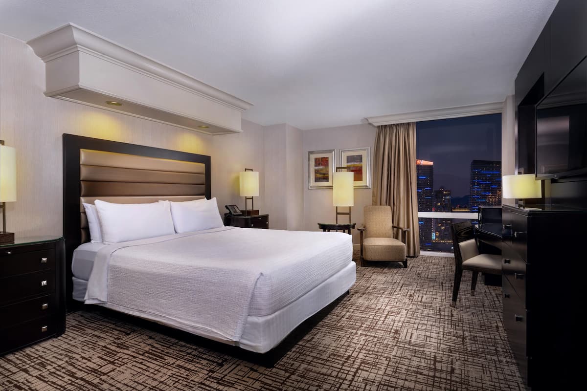A hotel room with a large bed, a desk, a chair, and a TV.