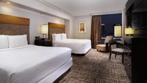A hotel room with two beds, a desk, a chair, a TV, and a city view.