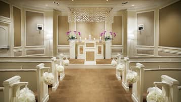 Ein festlicher Innenraum mit einem zentralen Altar, weißen Blumendekorationen und einem beige farbenen Teppichboden.
