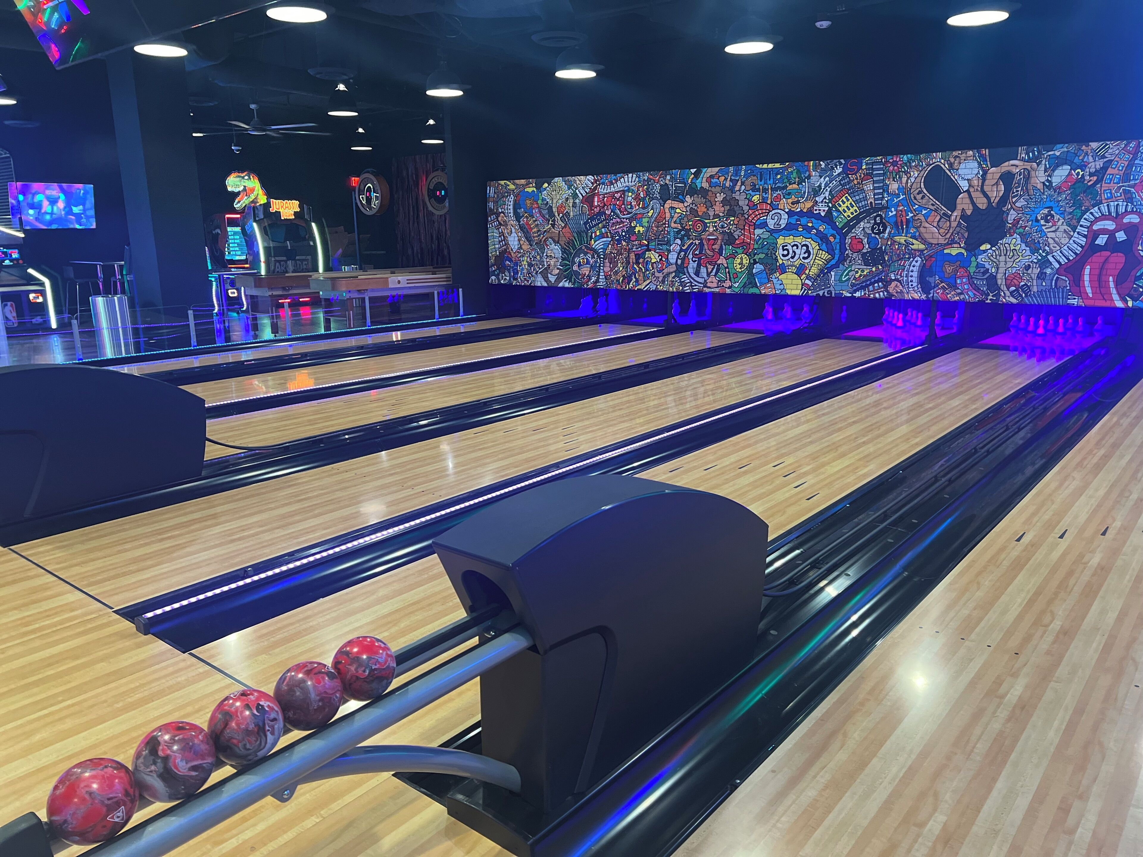 A bowling alley with multiple lanes, a colorful mural on the wall, and a digital scoreboard.