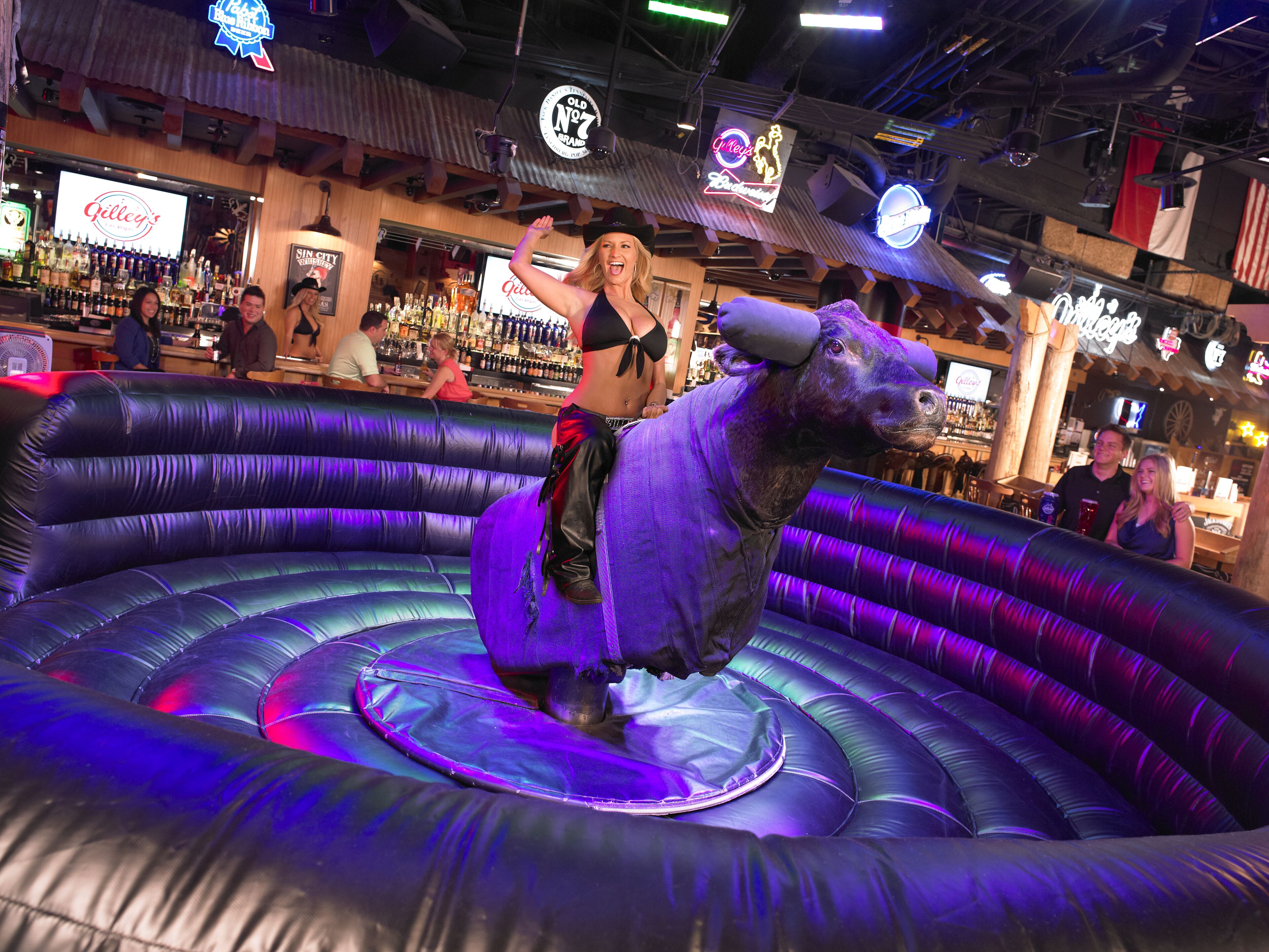 A bar with a neon sign, a large inflatable bull, and people in the background.