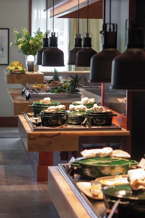 A buffet setup with multiple serving stations, green serving containers, and hanging pendant lights.