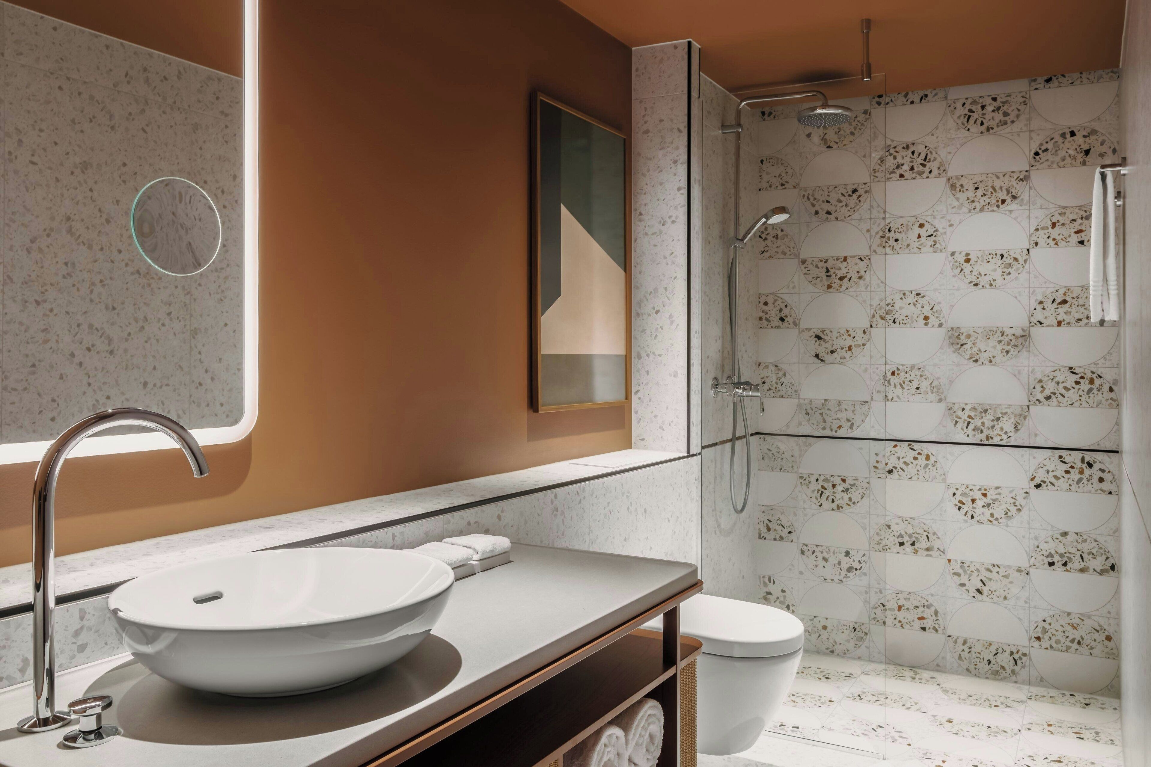 Et moderne badeværelse med en stor skålhåndvask, en bruseniche med glasdør og et toilet.