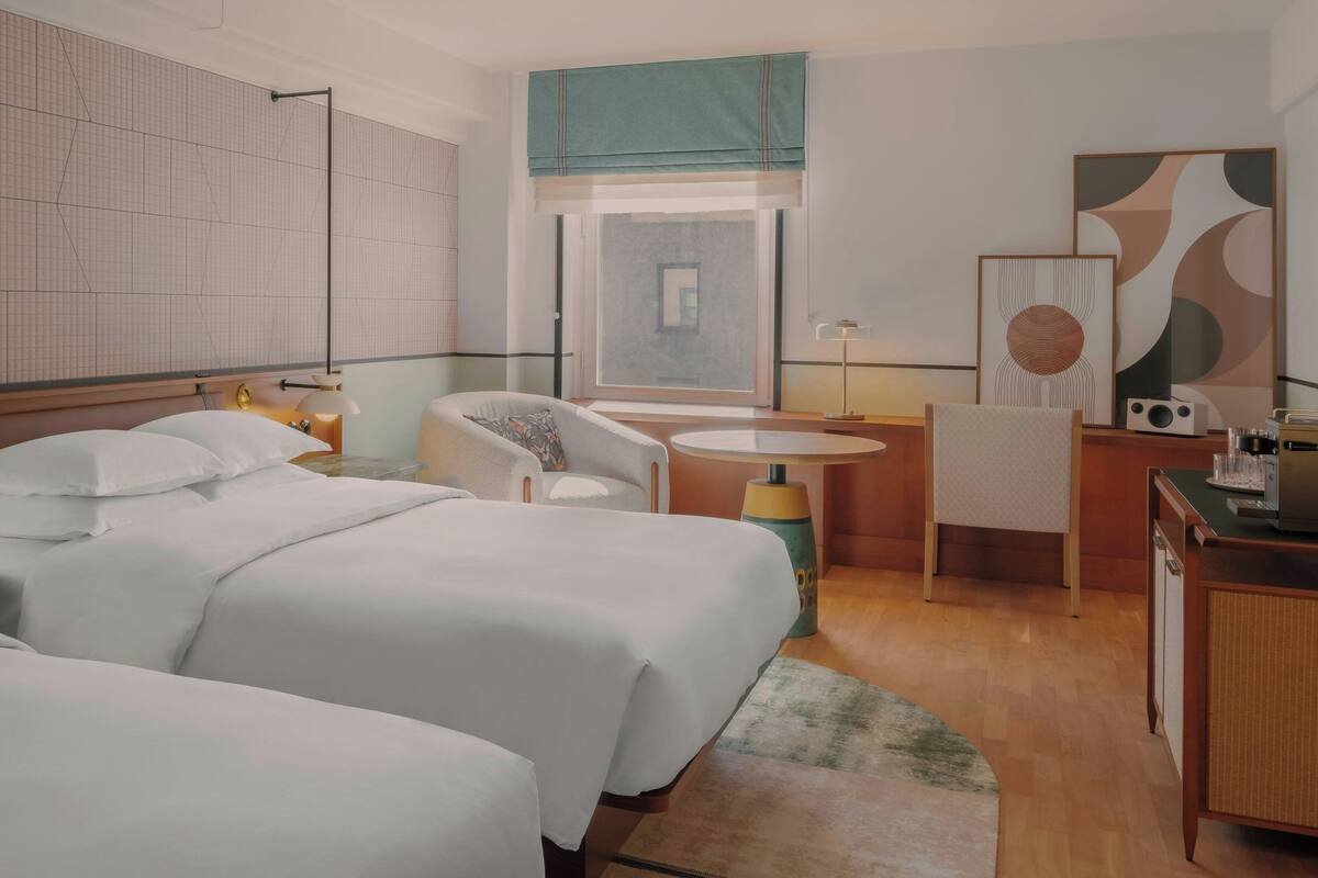 A hotel room with a large bed, a desk, a chair, a small table, and a window with a view.