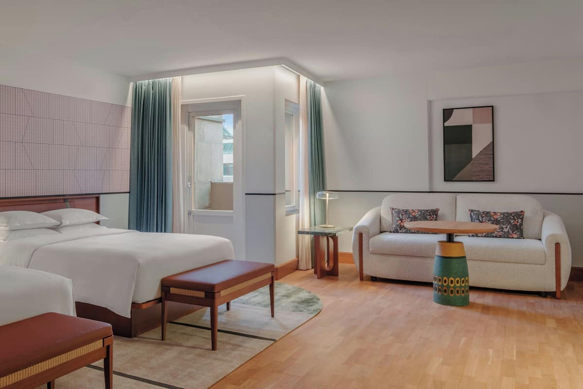 A hotel room with two beds, a sofa, a small table, and a lamp.