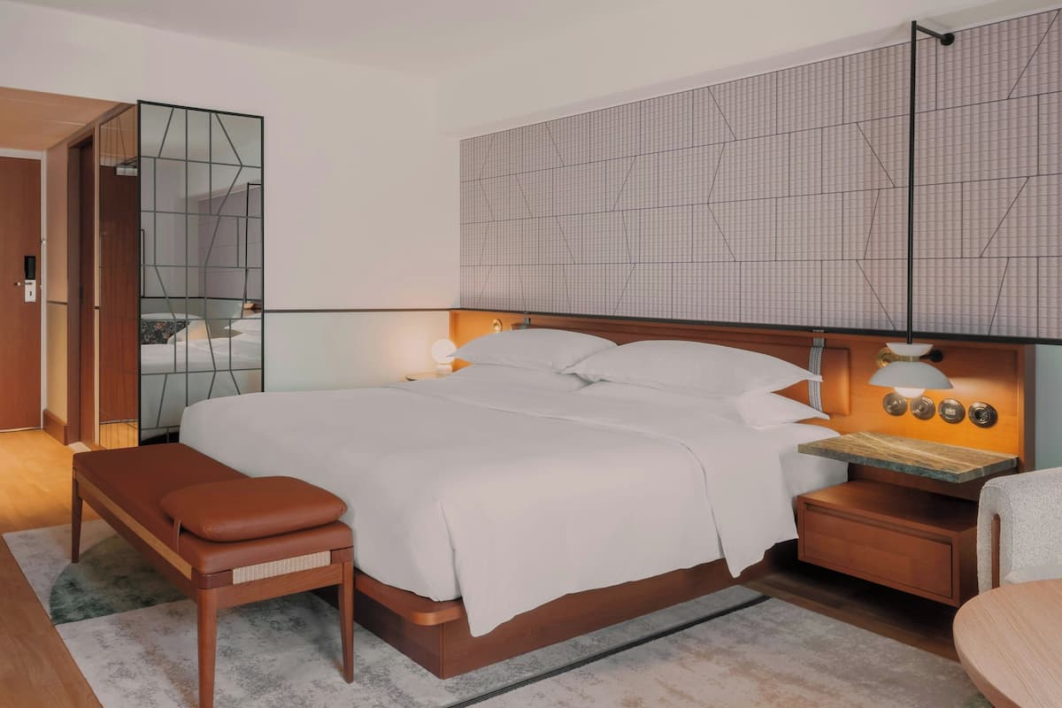 A modern bedroom with a large bed, bedside tables, a bench, and a mirror.