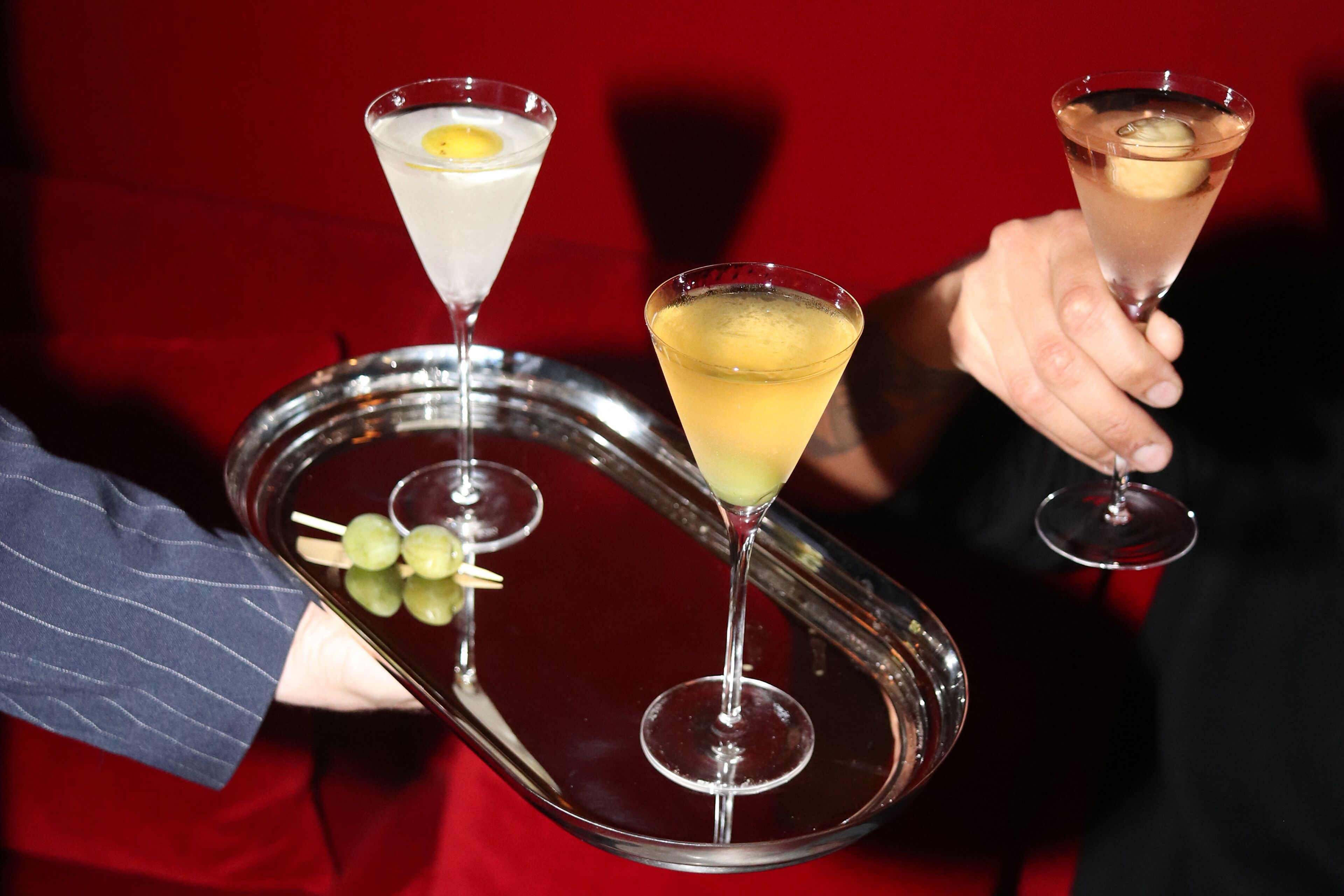 Una bandeja con dos copas de martini, una con una rodaja de limón y otra con una cereza, sostenida por una persona.