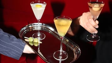 Una bandeja con dos copas de martini, una con una rodaja de limón y otra con una cereza, sostenida por una persona.