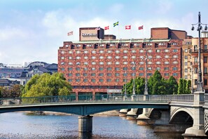 A hotel with a brick facade, a bridge in the foreground, and flags on the roof.