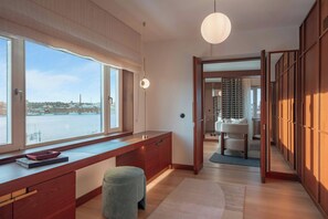 Quarto moderno com grande janela, escrivaninha de madeira e vista para a água.