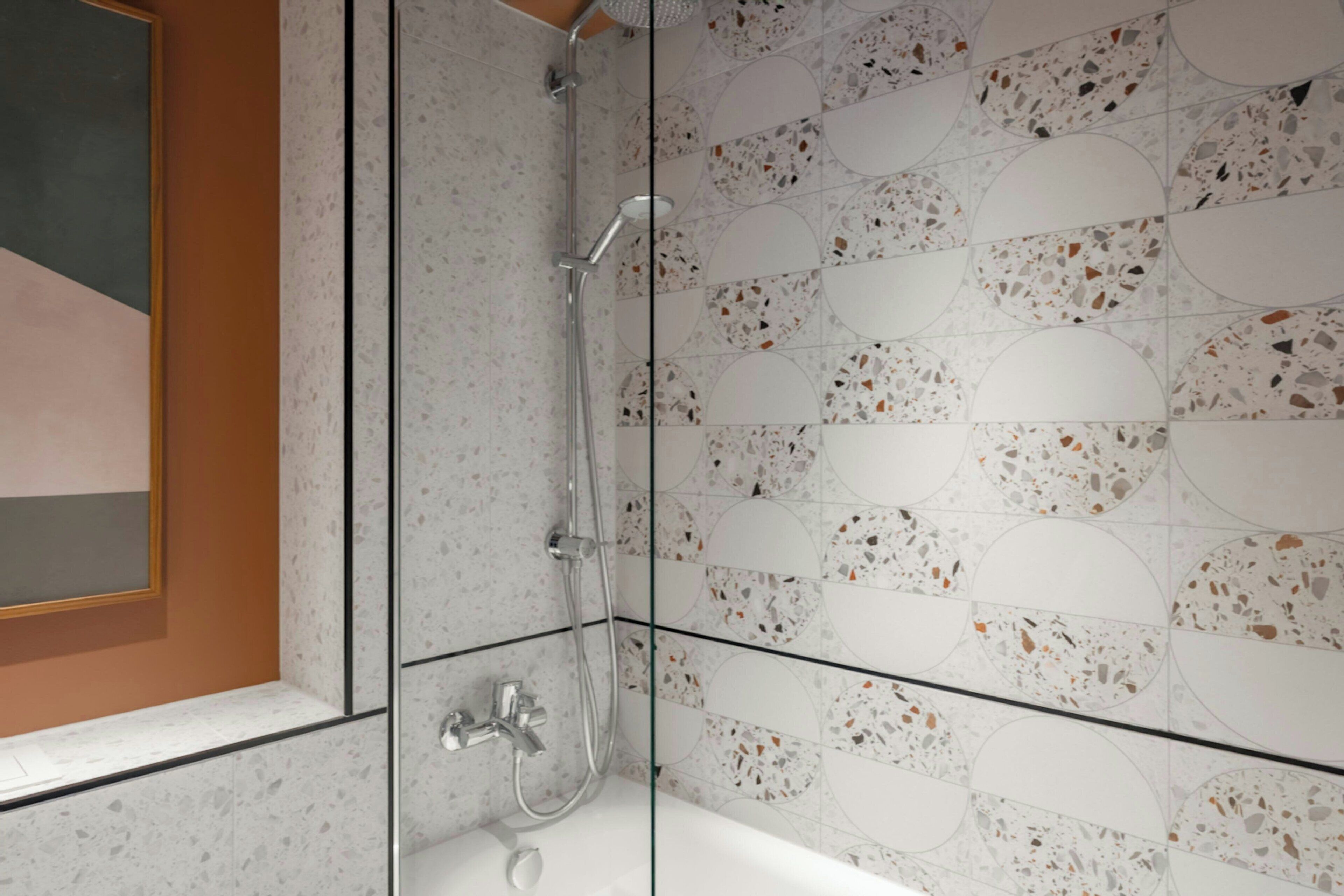 Ein modernes Badezimmer mit einer Duschkabine aus Glas, einer weißen Badewanne und Terrazzo-Wandfliesen.