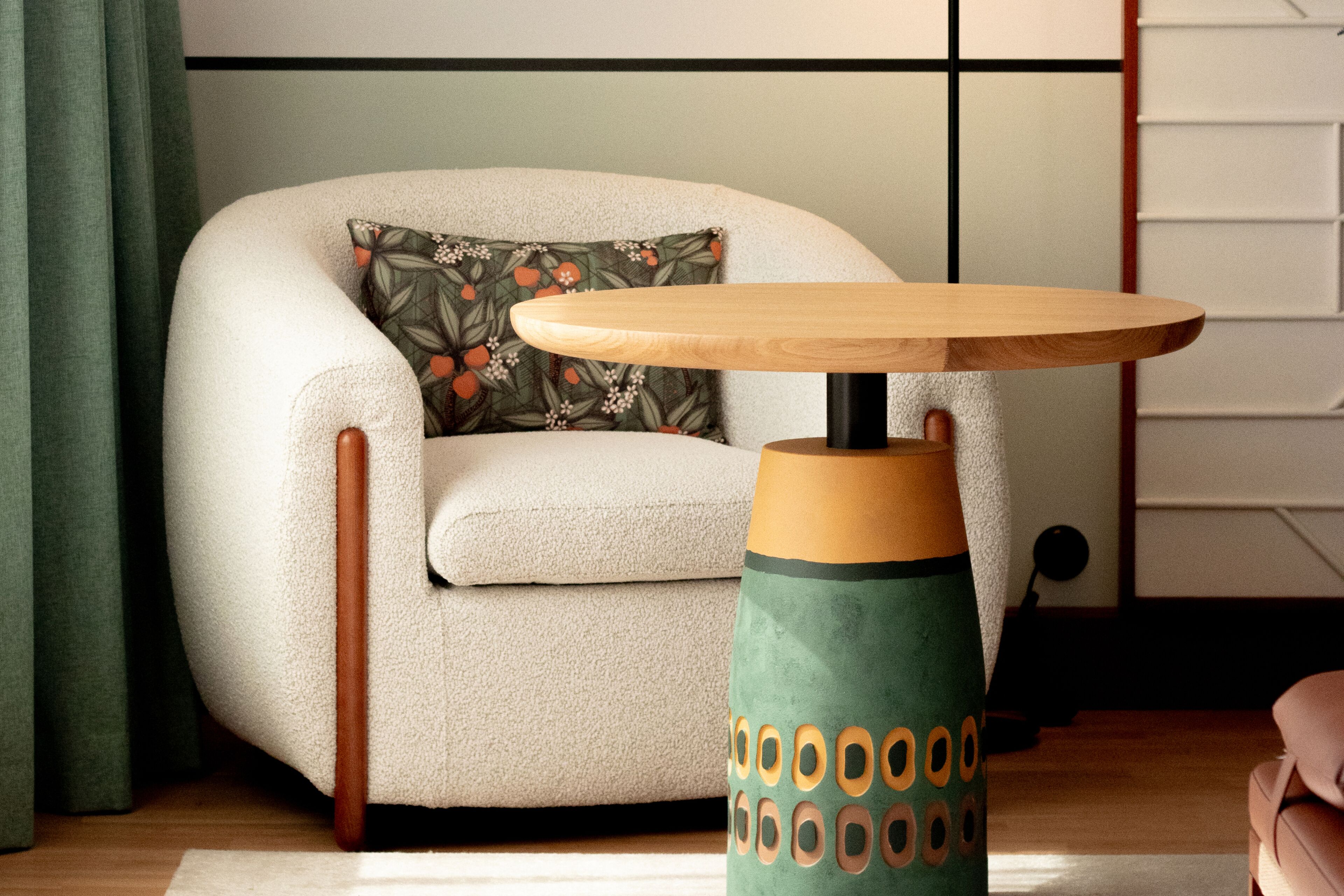 Ein Zimmer mit einem runden Holztisch, einem grün gemusterten Kissen und einem beigen Sofa.