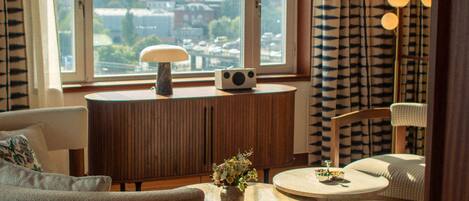 Un salón moderno con vistas a la ciudad, una mesa de centro redonda, un sofá y un mueble con un jarrón de flores.