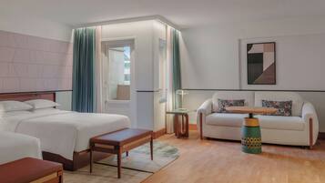 A hotel room with a bed, a sofa, a small table, and a lamp.