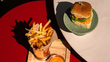 Una comida que incluye una hamburguesa y papas fritas sobre una mesa de madera, con un fondo rojo y blanco.
