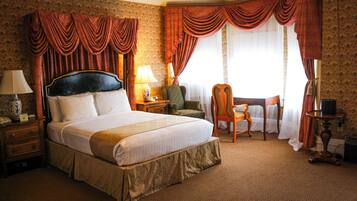 A hotel room with a large bed, a chair, a desk, and a window with curtains.