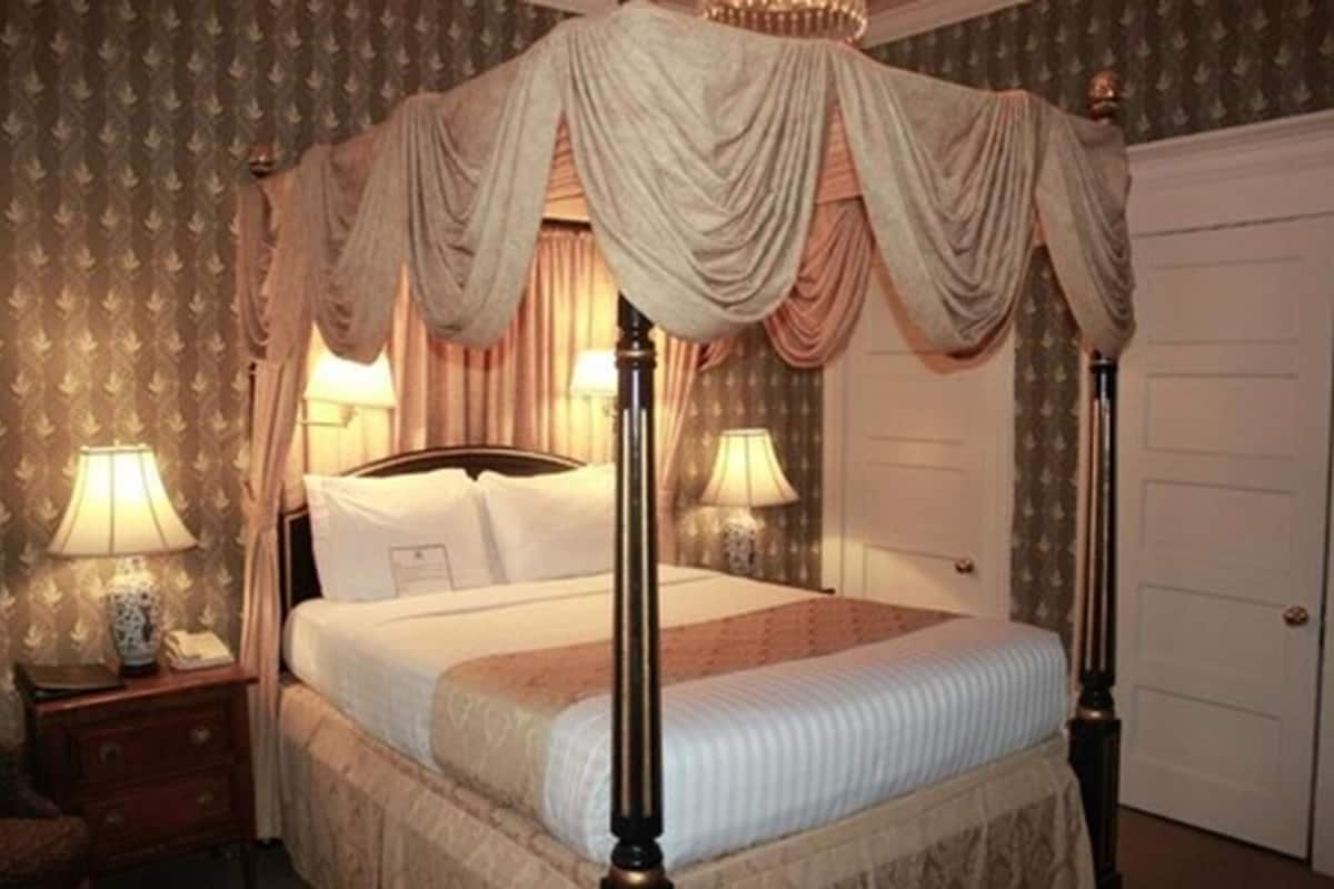 A four-poster canopy bed with a headboard, two bedside tables with lamps, and a door in the background.