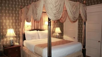 A four-poster canopy bed with a headboard, two bedside tables with lamps, and a door in the background.