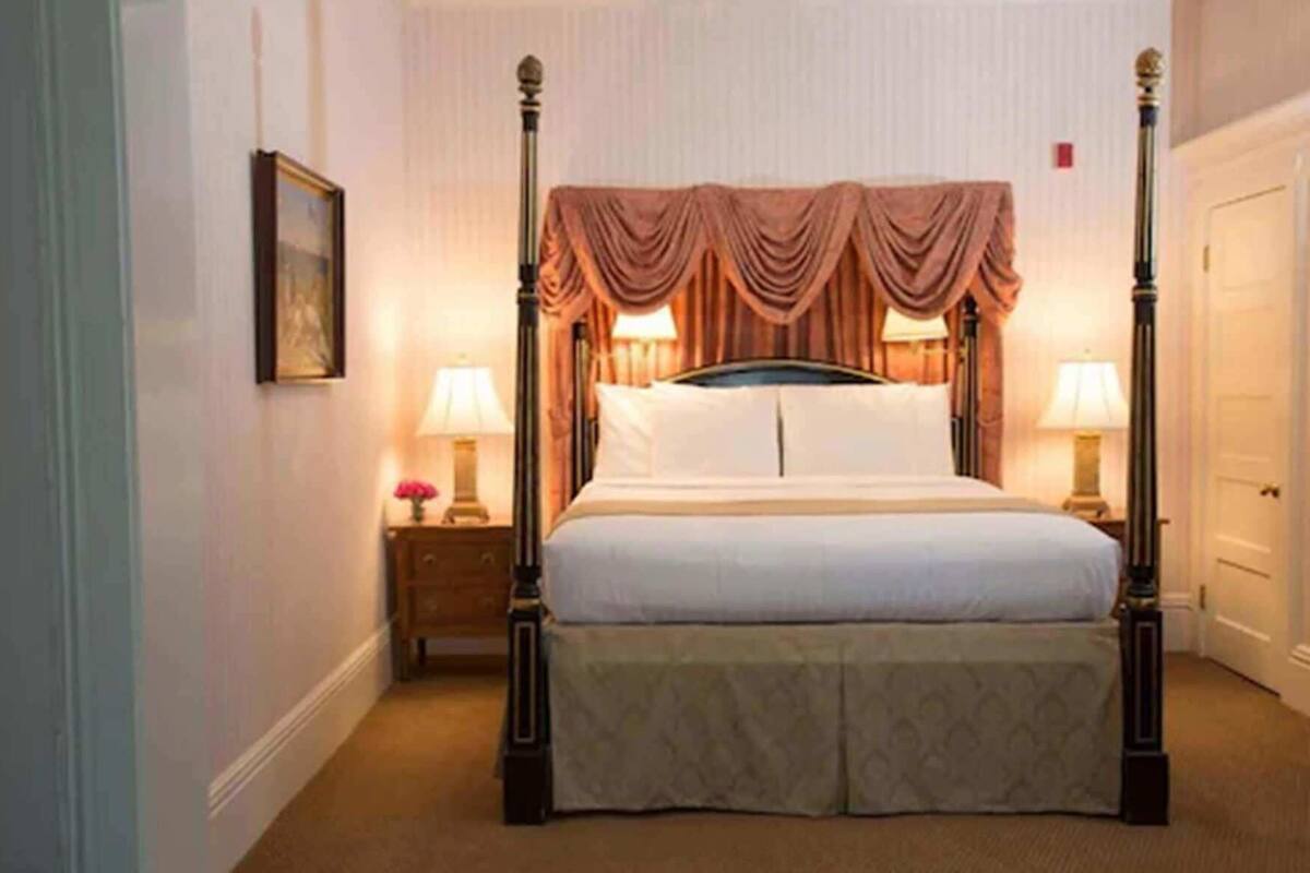 A four-poster bed with a canopy, a nightstand with a lamp, and a framed picture on the wall.