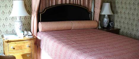 A bedroom with a bed, a nightstand, a lamp, and a patterned wallpaper.
