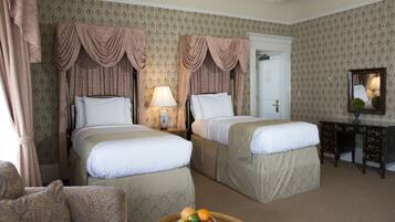 A hotel room with two beds, a desk, a chair, and a fruit bowl on a small table.