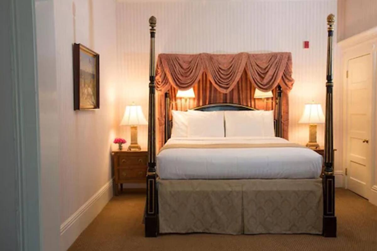 A four-poster bed with a canopy, bedside tables with lamps, and a framed picture on the wall.