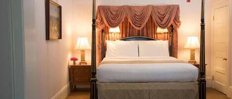 A four-poster bed with a canopy, bedside tables with lamps, and a framed picture on the wall.