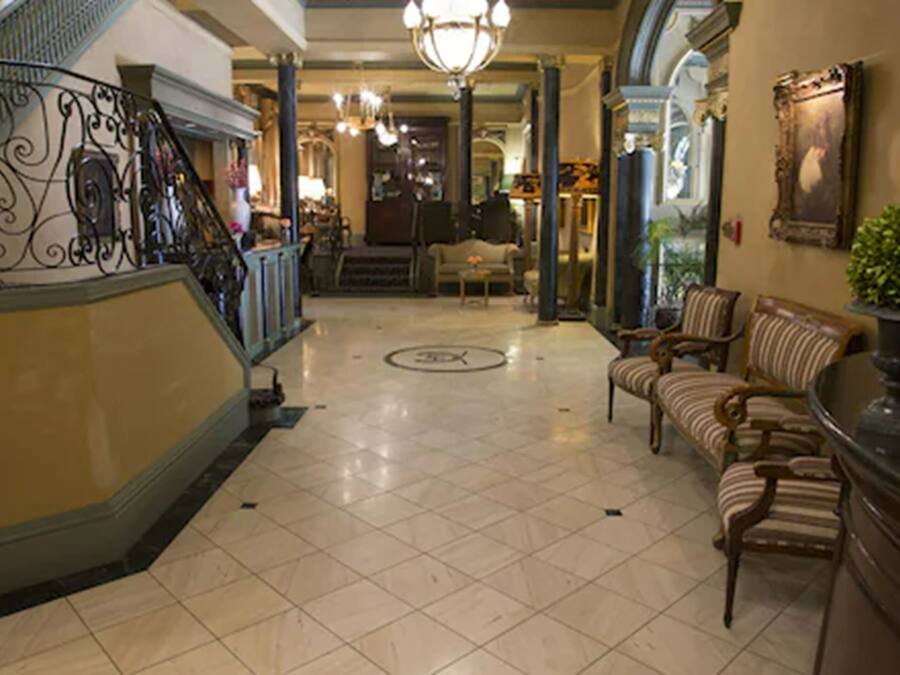 A grand lobby with a staircase, a chandelier, and a seating area with striped sofas.